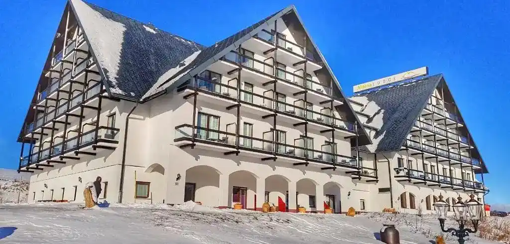 Das Hotel Alpina Lodge in Oberwiesenthal. Ein großes, weißes Gebäude mit dunkelfarbenen Balkonen und einem dicken