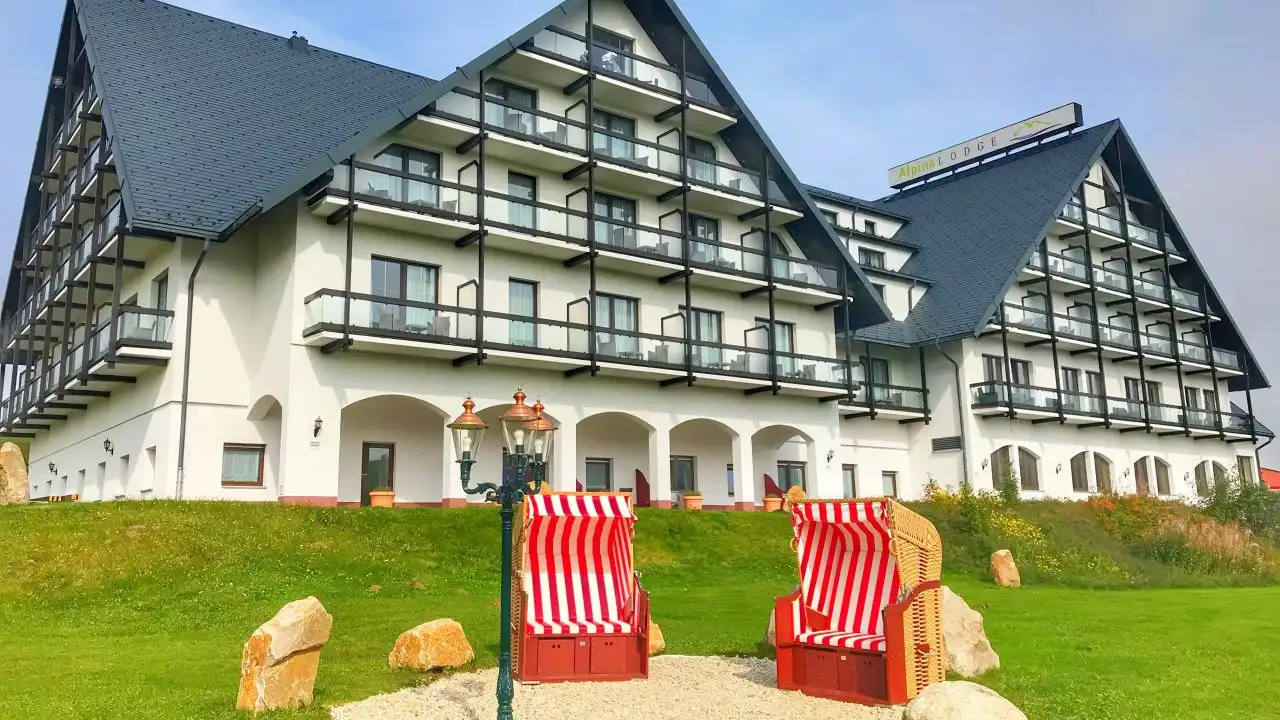 Das Hotel Alpina Lodge in Oberwiesenthal. Es ist ein großes, weißes Gebäude mit schwarzen Balkonen und einem dicken