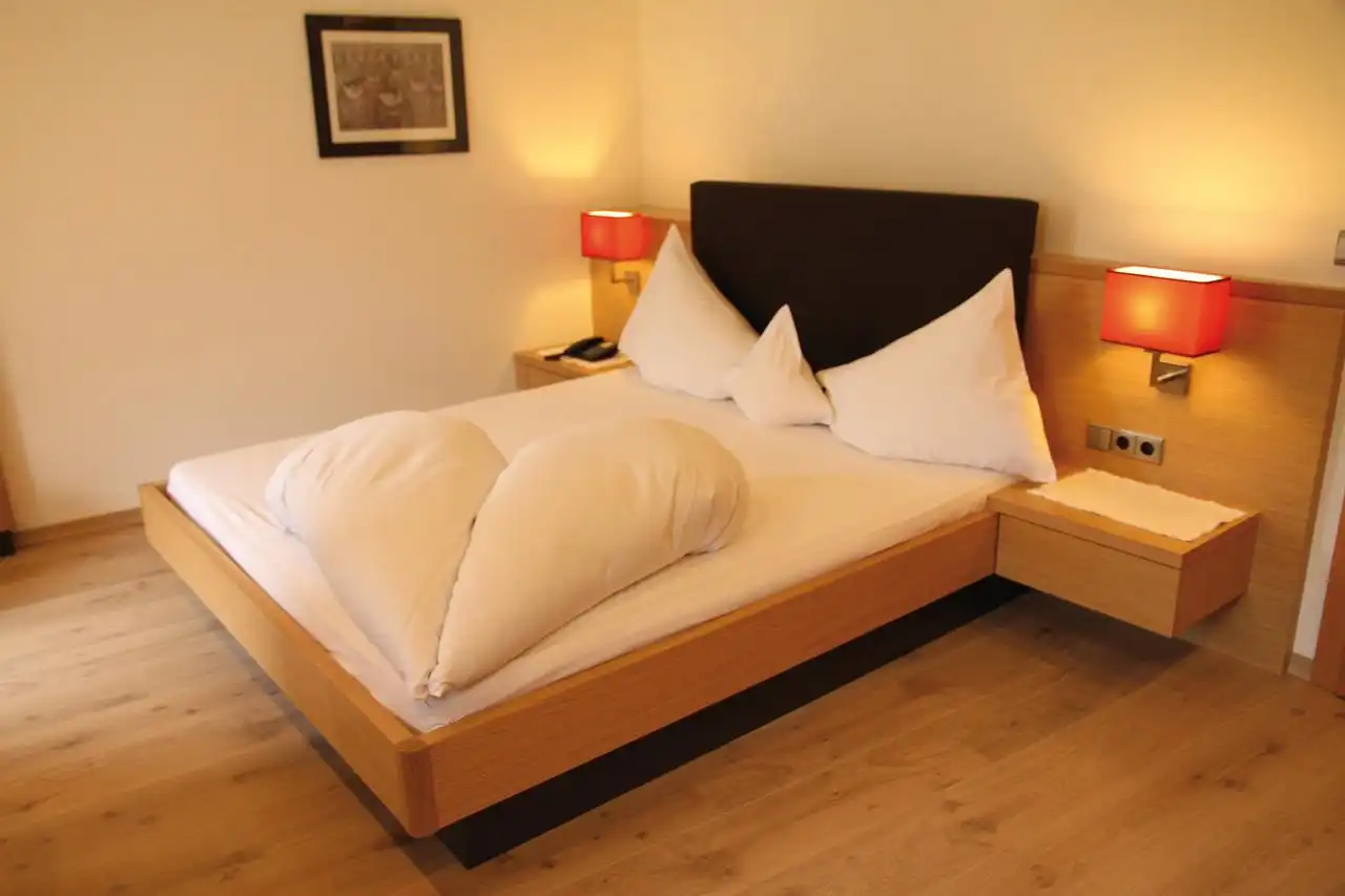 Ein gemütliches Zimmer im First Mountain Hotel Montafon. Das Bett mit weißen Laken und Kissen ist das Zentrum des Raumes,