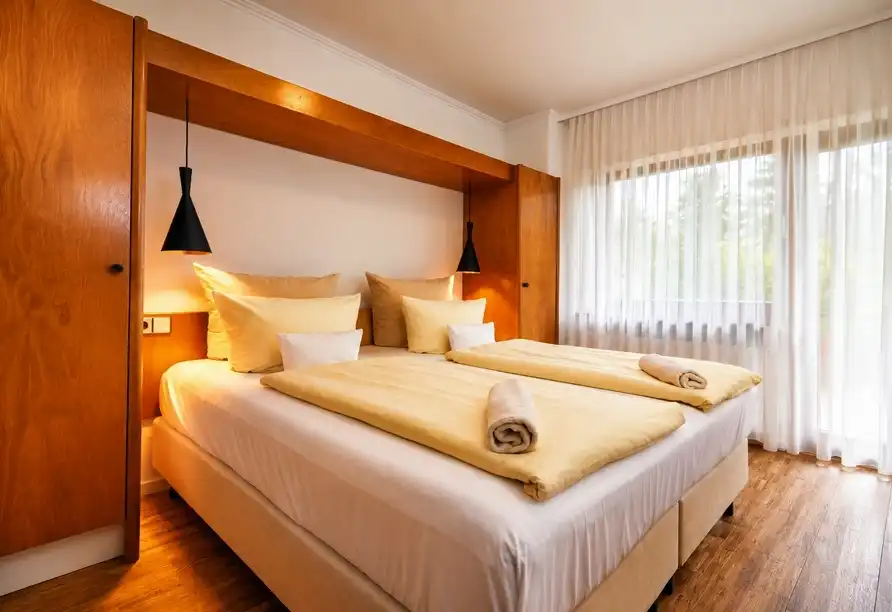 Ein Schlafzimmer mit einem Doppelbett, bequem gestaltet, mit goldenen Bettwäsche und weißen Vorhängen. Der Raum verfügt über