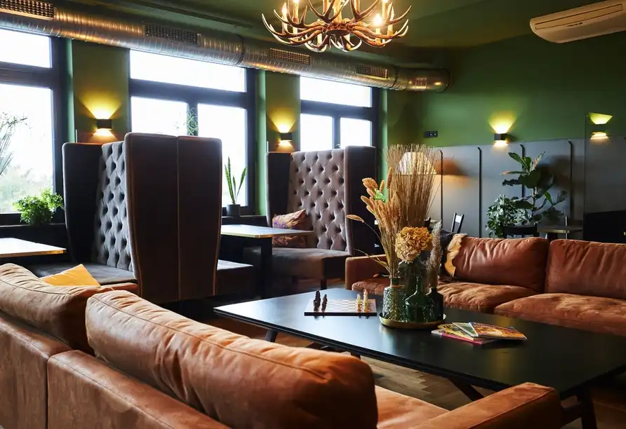 Ein Wohnzimmerbereich im Erck. Hotel & Gastronomie mit bequemen Sofas, einem Tisch und Dekorationen wie Pflanzen und Vasen.