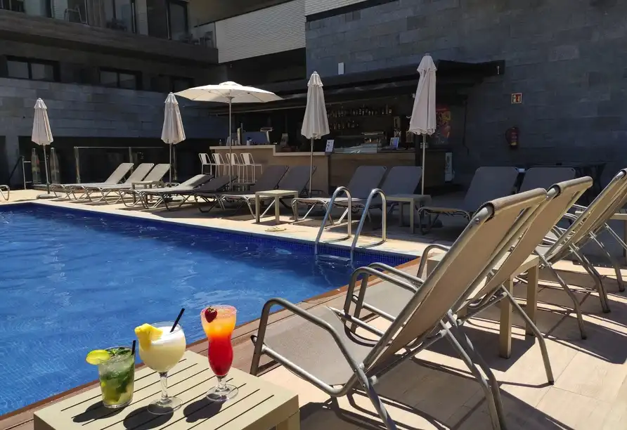 Einen Außenpoolbereich mit umliegenden Lounge-Stühlen und einem Barbereich. Die Lage scheint sich in einem Hotel oder Resort