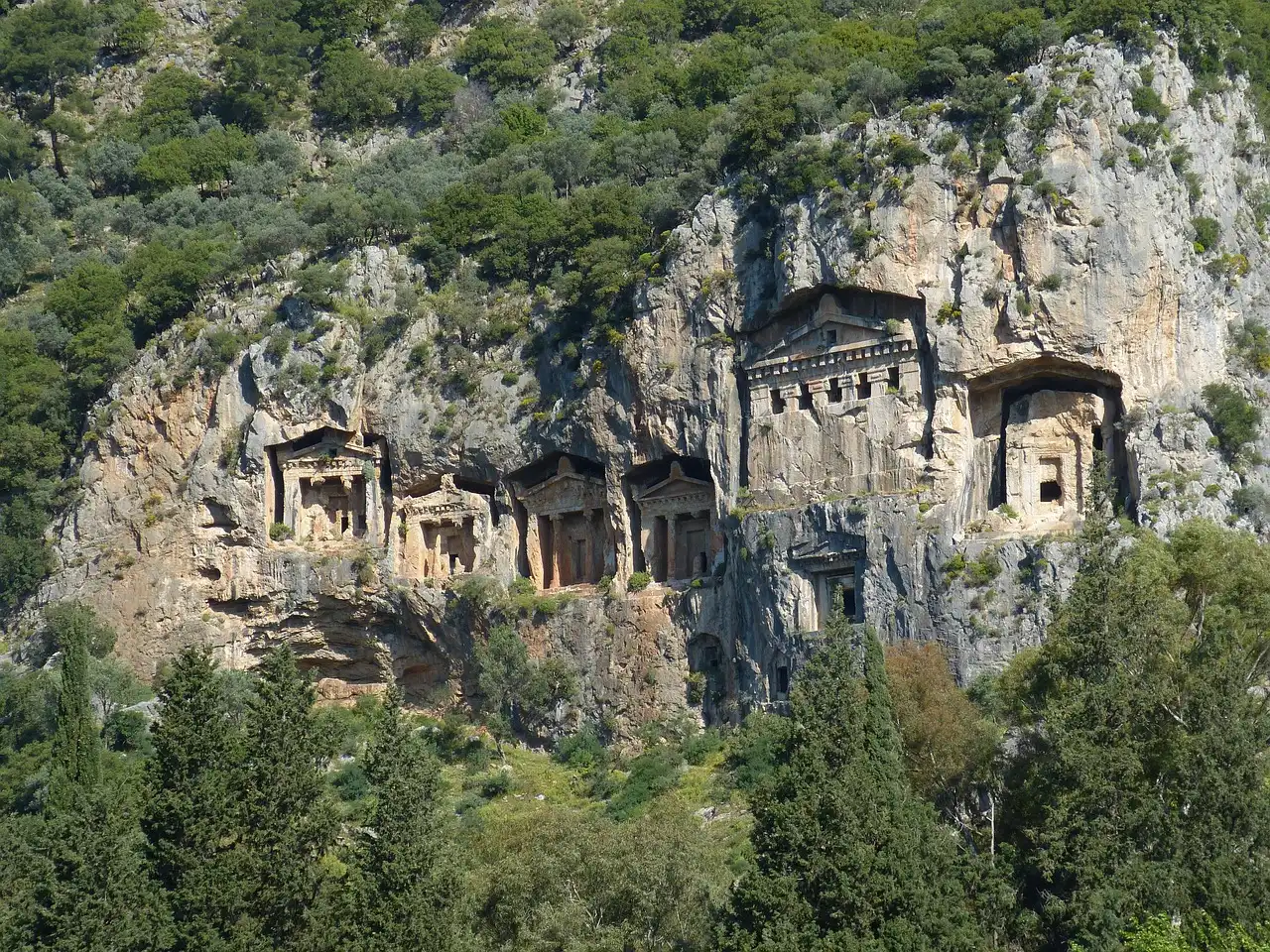 Die Bilder zeigt eine Felsgrube mit antiken Grabungen und architektonischen Strukturen in einem bergigen Gebiet. Die
