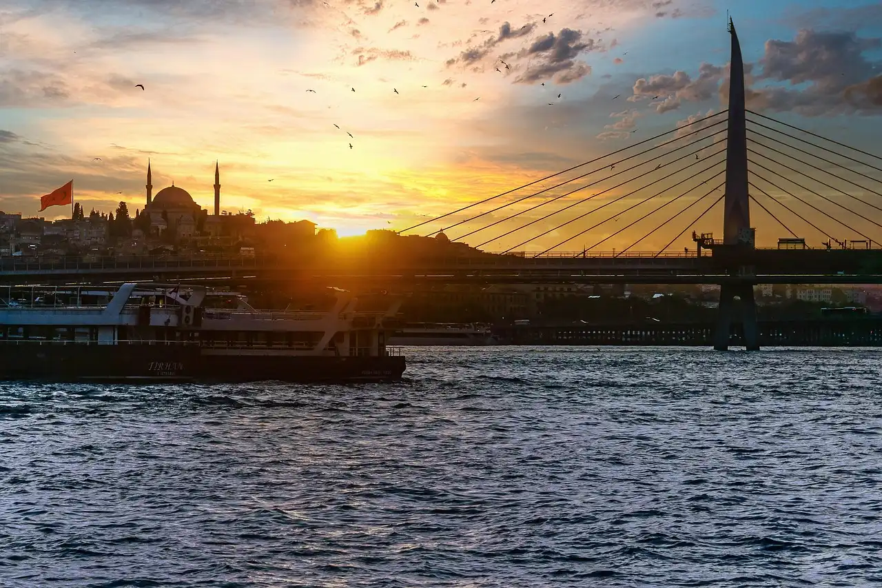Ein Boot fährt auf einem Fluss, während die Sonne untergeht, und ein majestätischer Hängebrücke im Hintergrund steht. Die