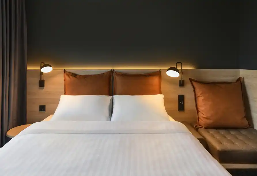 Ein Schlafzimmer im Hotel Moxy Dresden Neustadt mit einem doppelten Bett, bequemen Lichtern und einem modernen Ambiente