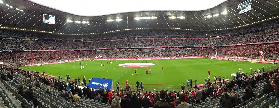 Ein Fußballspiel in der Allianz Arena. Die Szene zeigt eine große Fußballfläche mit Spielern, die sich auf dem Platz