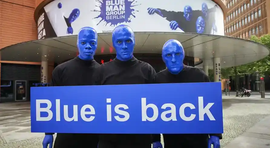 Die Bilder zeigen drei Menschen mit blauen Gesichtern und Händen, die einen Banner mit der Aufschrift "Blue is back" halten.