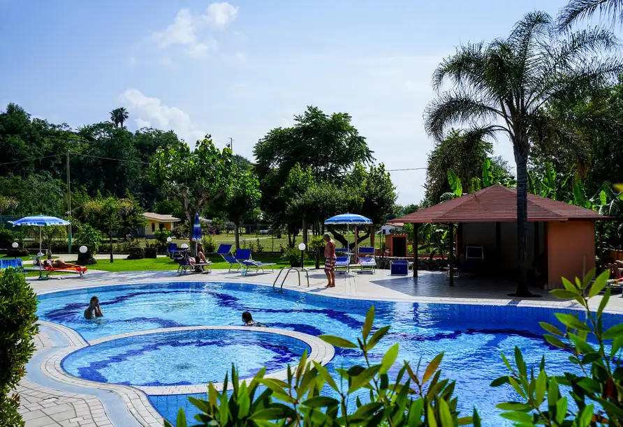 Einen Außenpool mit klaren blauen Gewässern. Um den Pool herum sind mehrere Liegestühle und Regenschirme platziert, einige