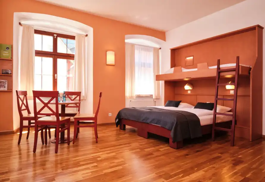 Ein Zimmer im JUFA Hotel Meersburg am Bodensee mit Holzböden, orangefarbenen Wänden und einem Fenster mit weißen Vorhängen.