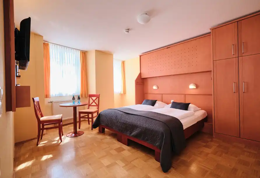 Ein Zimmer im JUFA Hotel Meersburg am Bodensee. Das Zimmer verfügt über ein großes Bett mit einem schwarzen Decken und zwei