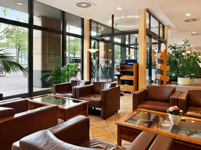 Ein Loungebereich im Flemings Hotel Bremen Bahnhofsplatz. Es gibt mehrere braune Ledersessel und Sofas, die um Holentische
