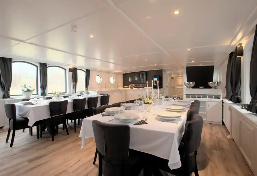 Eine elegante Esszimmer auf einem Schiff. Die Dekoration ist minimal und stilvoll, mit weißen Tischenläufern, schwarzen