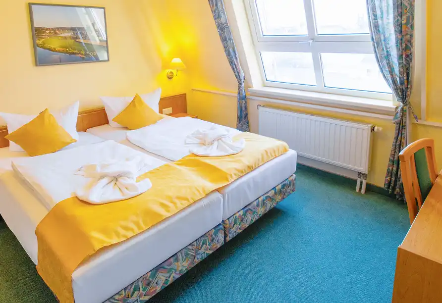 Ein Zimmer im Hotel Porzellanstadt Meißen. Das Zimmer verfügt über ein großes Bett mit weißem und gelben Bettwäsche, die