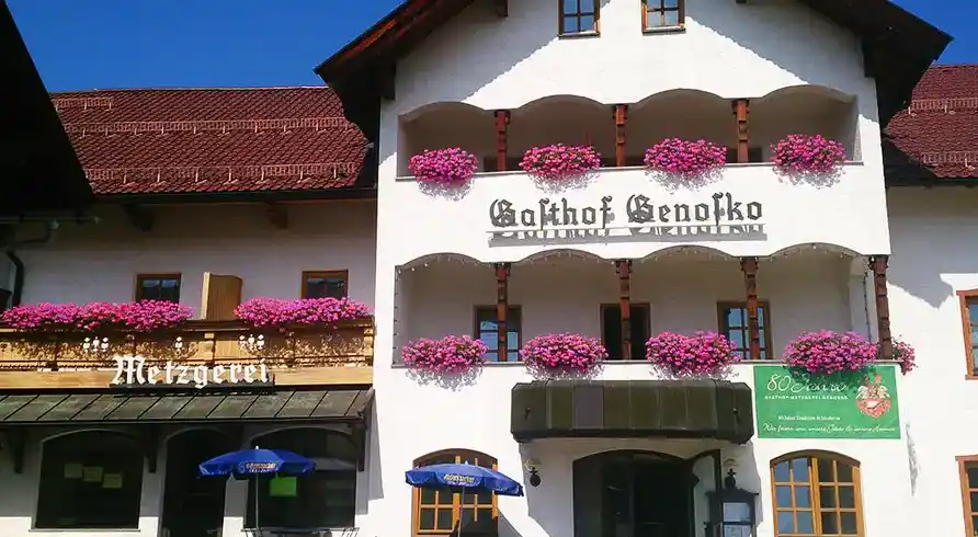 Das Gasthof Genosko in Spiegelau im Bayerischen Wald. Das Gebäude ist weiß mit roten Dächern und hat mehrere Balkone mit