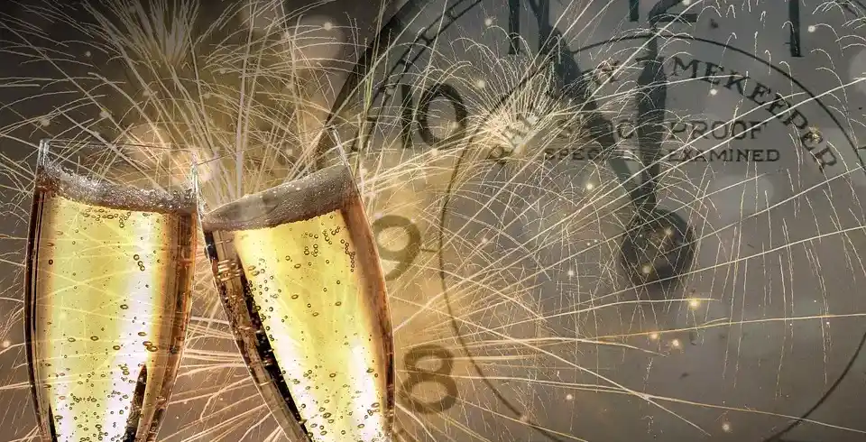 Zwei Gläser mit Sekt, die mit Schampferbenzüge gefüllt sind, während ein Silberuhrzeiger auf zwölf zeigt, umgeben von