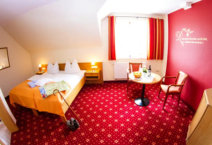Ein Zimmer im Landgasthof Wüllner in Winterberg mit einem Bett, einem Nachttisch mit Lampe, einem Schreibtisch mit Stuhl,