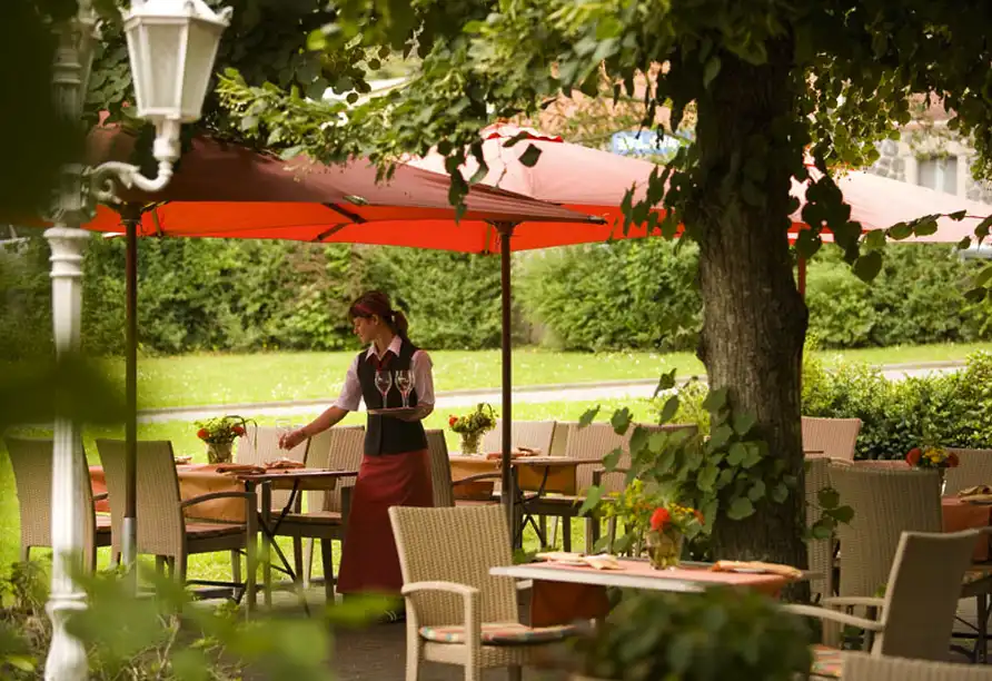 Ein Restaurant im Hotel Eisbach in Ransbach-Baumbach mit außenstehenden Tischen unter einem roten Sonnenschirm. Die