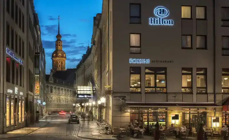 Eine beleuchtete Straße in Dresden, mit der großen Frauenkirche im Hintergrund. Links ist ein Hotel sichtbar, das Hilton