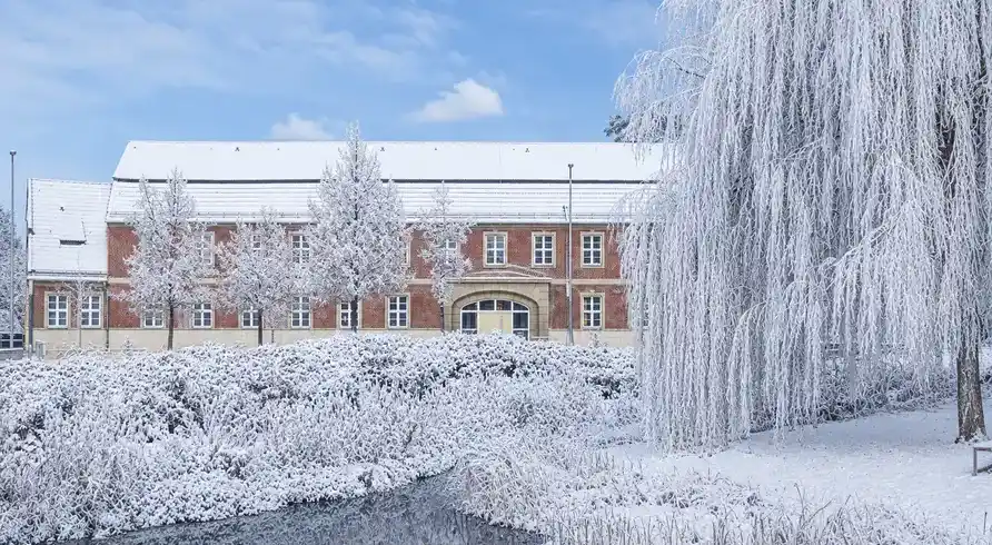 Ein Winterlandschaftsbild mit einem großen Gebäude, das Hotel VIERSEITHOF in Luckenwalde. Der Himmel ist blau mit weißen