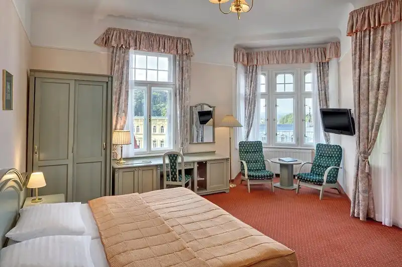 Ein Zimmer im Ensana Svoboda Health Spa Hotel in Marienbad mit einem Bett, einem Arbeitsbereich und einem Fernseher ist zu