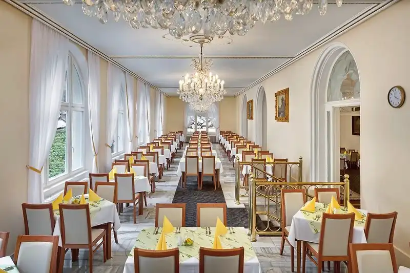Ein luxuriöses Restaurant mit weißem Ambiente, goldenen Details und einem großen Hintergrundfenster, das einen Blick auf die
