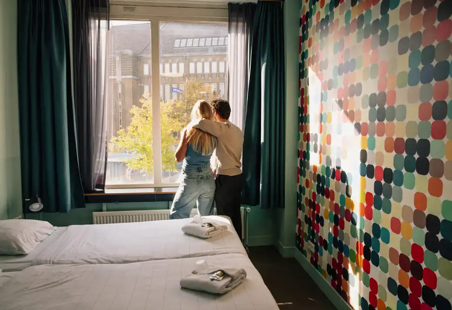 Paar blickt aus dem Hotelzimmerfenster im Stayokay Utrecht Center mit buntem Wanddesign