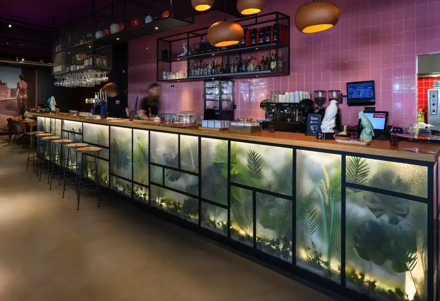 Stylische Hotelbar im Stayokay Utrecht Center mit grüner Dschungel-Deko und rosa Fliesen