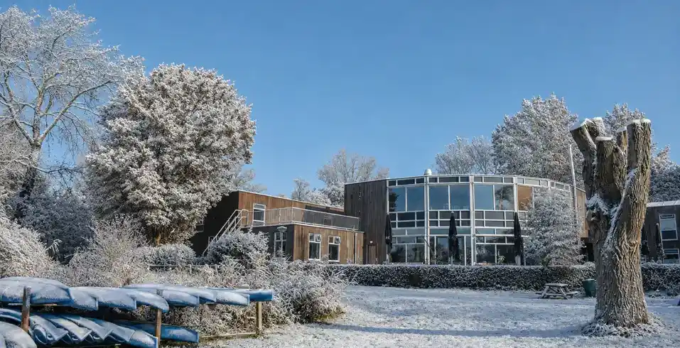 Winterliche Außenansicht des Stayokay Hostel Dordrecht mit verschneiten Bäumen am Wasser