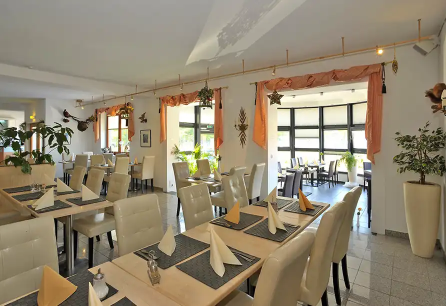 Ein elegantes Restaurant mit weiß gekleideten Tischen und orangefarbenen Vorhängen. Die Atmosphäre ist einladend und lädt zu