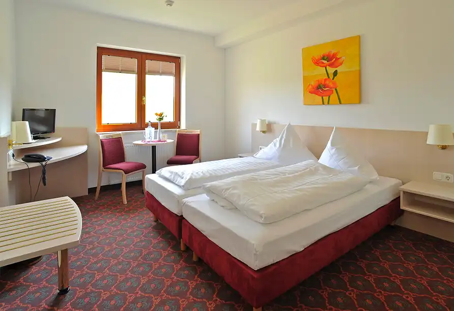 Ein Zimmer im Hotel Quickborn in Quickborn. Das Zimmer verfügt über zwei Betten, eine weiße Bettwäsche und rote