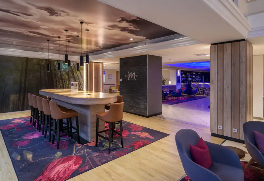 Ein Lounge im Hotel Reitenberger in Marienbad mit einem langen Tisch und mehreren Stühlen. Die Dekoration umfasst rote und