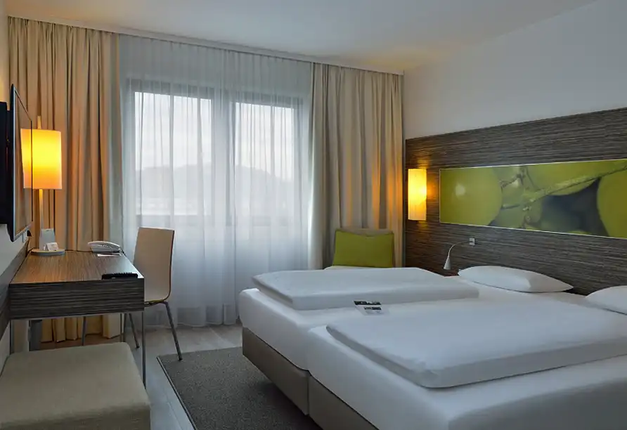 Ein modernes Hotelzimmer mit einem Blick auf den Außenbereich. Das Zimmer verfügt über zwei Betten, einen Arbeitsplatz mit