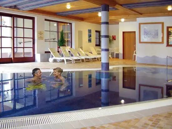 Einen Indoorpool im Hotel Bad Hochmoos. Zwei Personen schwimmen im Pool. Das Hotel bietet Wellnessanlagen wie Hallenbad,