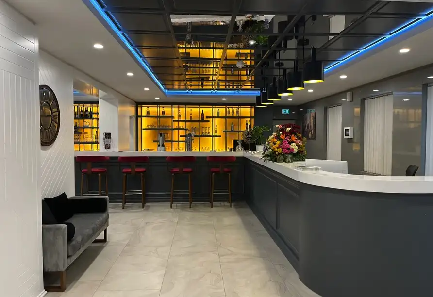Einen modern gestalteten Barbereich mit einem großen Bar-Tresen, auf dem rote Stühle platziert sind. Im Hintergrund ist eine