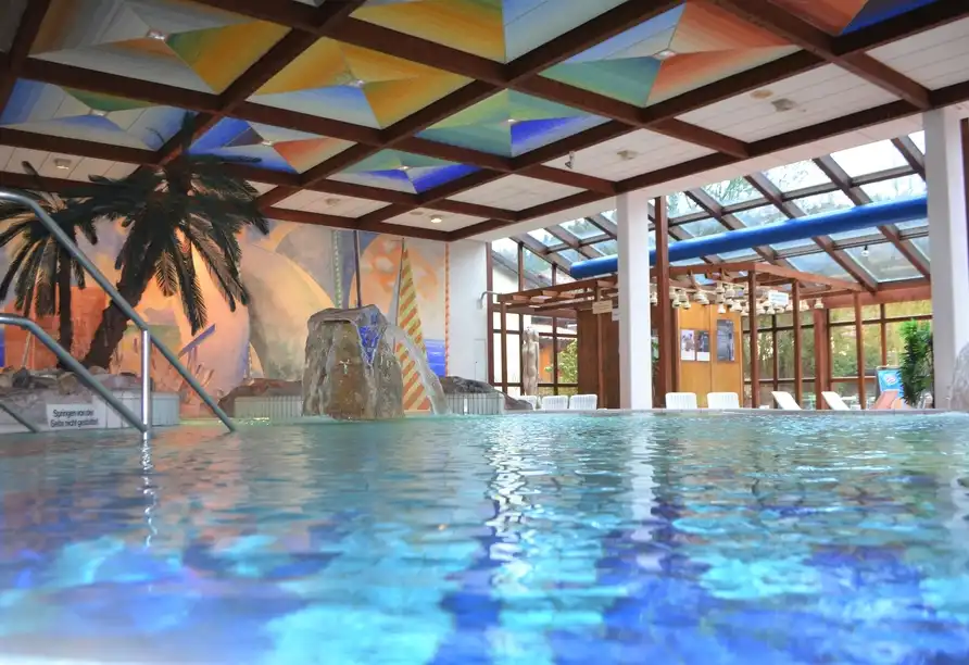 Einen Indoorpool des Hotels WAGNERS Steinwiesen. Der Pool ist mit leuchtend blauen Wasser gefüllt und wird von einem