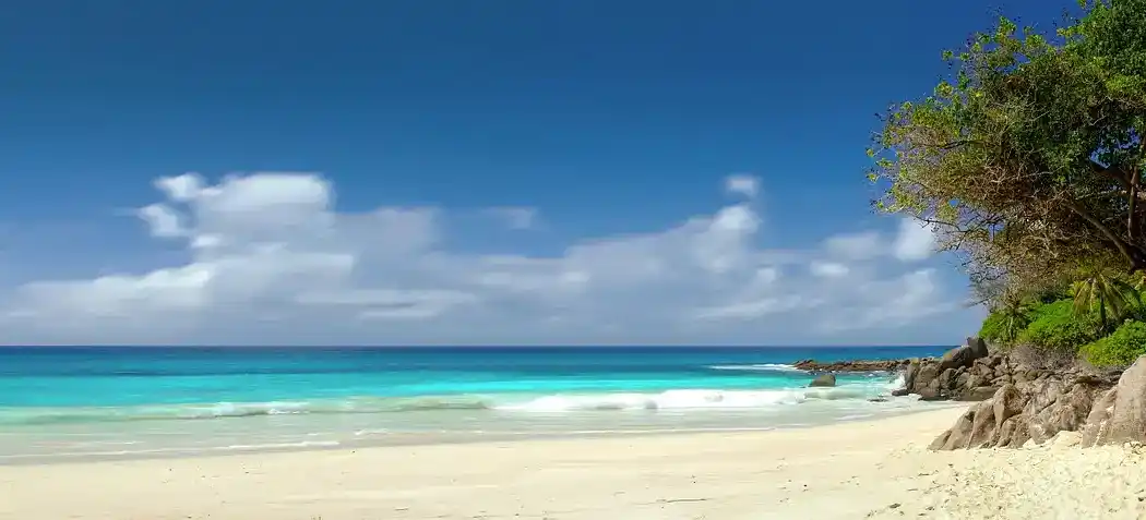 Eine schöne weiße Strandstrasse mit klaren blauen Gewässern und einem üppigen grünen Ufer. Der Himmel ist klar und blau, mit